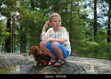 Long-haired Dachshund, Long-haired sausage dog, domestic dog (Canis lupus f. familiaris), nine years old boy crouching with a dachshund on a skerry, portrait of a child, Sweden, Smaland, Loftahammer Stock Photo