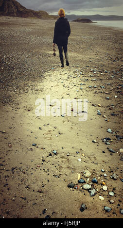 woman walking in distance on the beach holding  drift wood Stock Photo