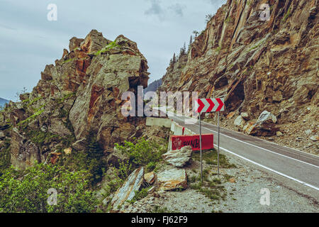 Picturesque mountain landscape with roadside red and white triple chevron sign warning for dangerous road turn on sinuous Transf
