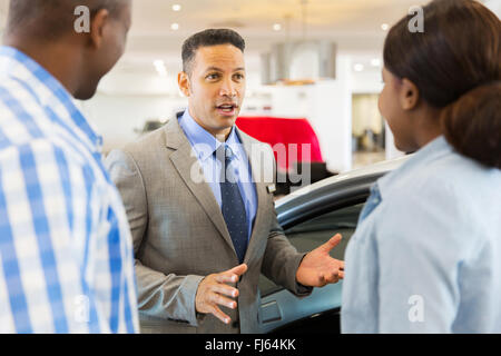 middle aged car salesman talking to African couple inside showroom Stock Photo