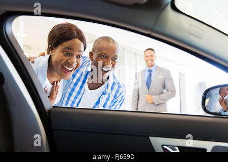 happy African couple choosing luxury car at vehicle dealership looking at the interior Stock Photo