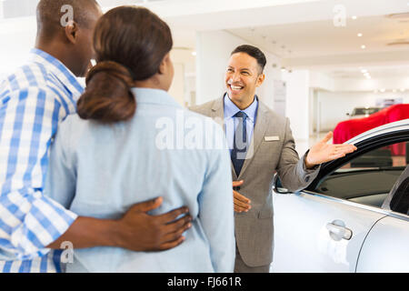 friendly car dealer showing new car to customers Stock Photo