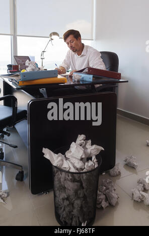 Corporate manager in modern office tries to write a job letter. The man is frustrated and keeps on throwing paper on desk and tr Stock Photo