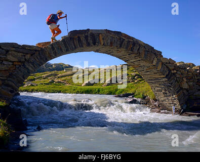 wanderer crossing old arch bridge, France, Savoie, Vanoise National Park, Evettes Stock Photo