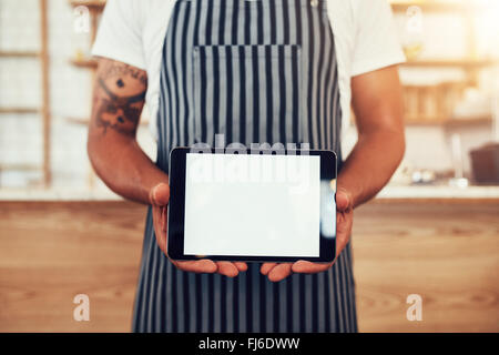 Close up shot of a man wearing an apron showing a digital tablet. Male barista holding a touch screen tab with copy space for yo