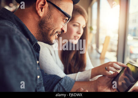 Happy young man with his girlfriend in a coffee shop surfing internet on digital tablet. Young couple in a restaurant looking at