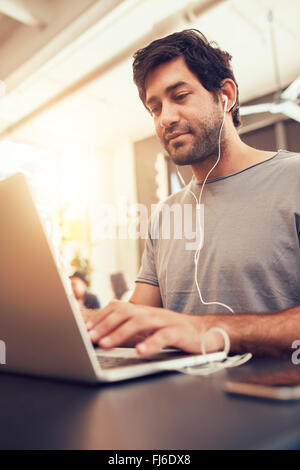 Portrait of young man looking busy working on laptop at a cafe. Caucasian man sitting in coffee shop using laptop. Stock Photo