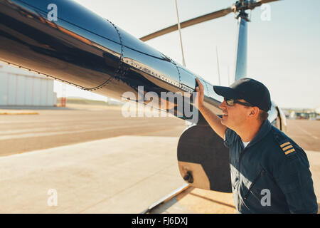 Male pilot checks the tail of helicopter before the flight. Mechanic checking helicopter before take off. Stock Photo