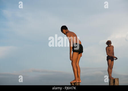 AMARAPURA, Myanmar — U Bein Bridge stretches across Taungthaman Lake near Mandalay. The 1.2-kilometer-long teakwood structure, believed to be the oldest and longest teakwood bridge in the world, is silhouetted against the sky. Local pedestrians and monks cross the bridge while tourists observe the iconic scene, particularly popular during sunset. Stock Photo