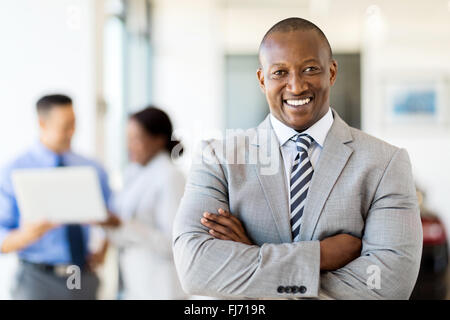 happy African salesman standing at car dealership with colleagues on background Stock Photo