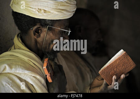 Orthodox priest holding a cross and reading Holy Book inside Mikael Milhaizengi rock-hewn church in the Tigray Region, Ethiopia Stock Photo