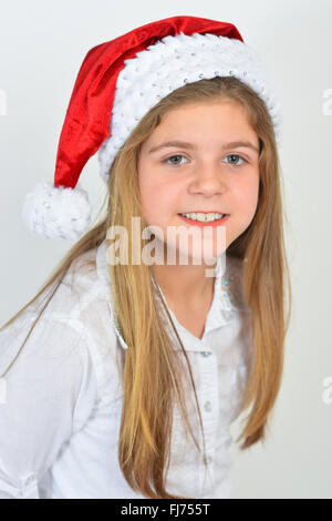 Adorable young girl wearing a Christmas hat while posing, against white background. Stock Photo