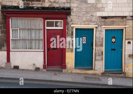 Three front doors (1 red, 2 blue) side by side - these belong to small, quaint terrace cottages on Old Maltongate, Malton, North Yorkshire, England, Stock Photo