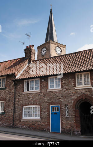 Spire of St Leonard and St Mary Roman Catholic Church, Malton, North Yorkshire, England, towers over a small terraced cottage with a blue door. Stock Photo