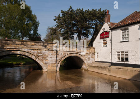 A waterside pub, the Rose Inn, (Pickering, North Yorkshire, England, UK) stands next to an old, stone arched bridge spanning Pickering Beck. Stock Photo