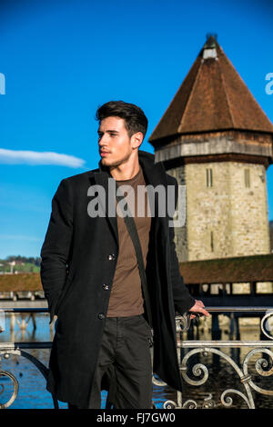 Handsome man standing near metal fence in Lausanne. Famous wooden bridge and Water Tower on background. Stock Photo