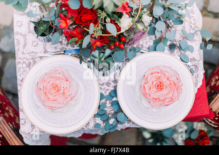 White wedding cake stylized as flower with red bouquet on wooden background Stock Photo