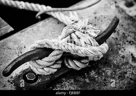 Nautical rope tied around horn cleat on dock, close up in black and white. Key West harbor, Florida. Stock Photo