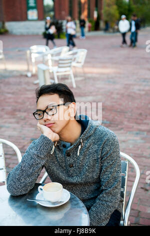 Young asian man in outdoor cafe with cup of coffee looking away being bored and unhappy Stock Photo