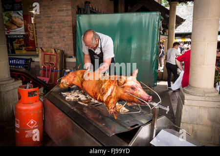 A man cutting meat from a roasted hog on a spit, Stroud Farmer's Market, Gloucestershire Stock Photo