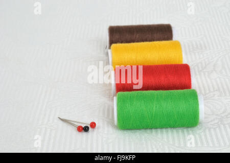 Spools of threads of different colors and needles on a light table Stock Photo