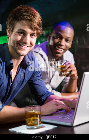 Two men having whiskey and using laptop at bar counter Stock Photo