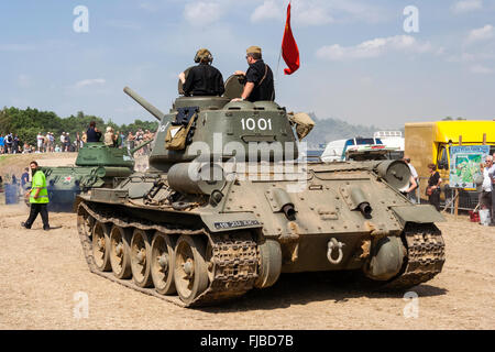 War and Peace show, England. Rear view of Second World War Russian T-34 tank driving along dusty dirt road towards show arena. Red flag on turret. Stock Photo
