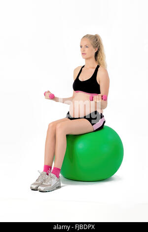 Pregnant woman on yoga balance ball performing bicep curl exercise with weights. Stock Photo