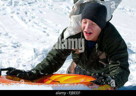 Cute teenager in toboggan riding down a tube on a snow hill laughing. Stock Photo