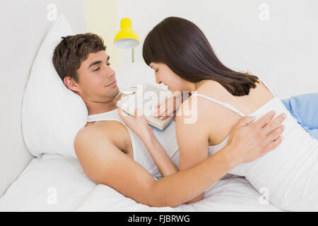 Woman lying on man and reading novel on bed Stock Photo