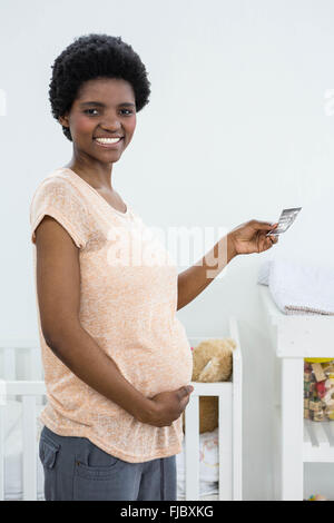 Pregnant woman holding ultrasound scan near baby cradle Stock Photo