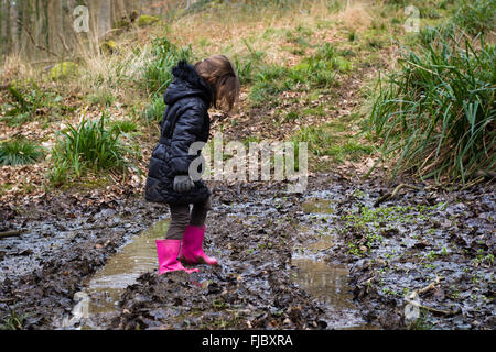 Child in mud on track through woodland. A young girl in pink wellies walks through mud in a British wood Stock Photo