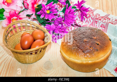 On the table are in a wicker basket painted Easter eggs, cake and artificial flowers. Stock Photo