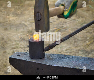 The work of a blacksmith. On vintage anvil by hammering heated metal, the blacksmith forges the product. Stock Photo