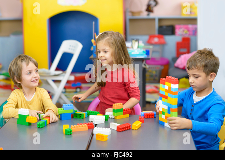 Three happy kids playing with plastic building blocks at kindergarten Stock Photo