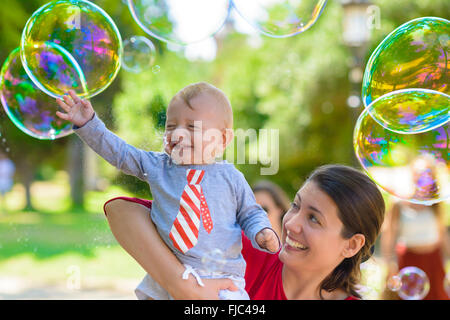 Cute baby and his mother catching soap bubbles in a summer day Stock Photo