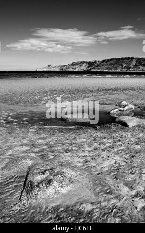 Rock pool and sand textures on quiet sandy beach, Runswick Bay, North Yorkshire Heritage Coast, summer, England UK, monochrome Stock Photo