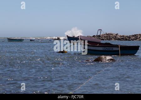 A small fishing boat moored securely in the sheltered harbour of Jacobsbaai while waves break on the rocks Stock Photo