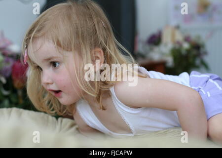 Closeup of a little blonde child kid girl, brown eyed two year old climbing on the couch Stock Photo
