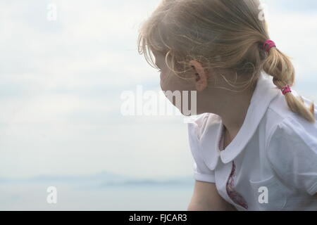 Little girl looking away from the camera out to the sea in the distance, blurred background, thinking concept, childhood concept Stock Photo