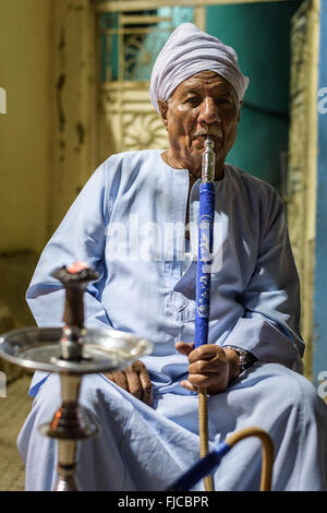 Old muslim man smoking from a water pipe outside a small restaurant at night. Stock Photo