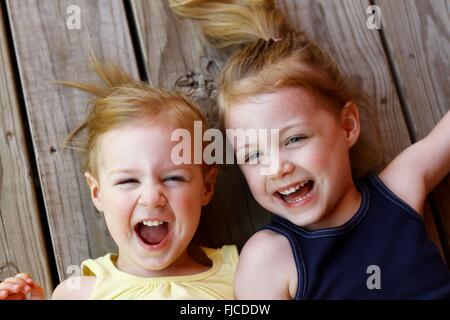 Two little girls lying on their backs laughing Stock Photo