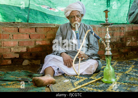 Old muslim man smoking from a water pipe sitting on a rug at Daraw camel market. Stock Photo