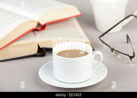 Cup of coffee on the table with two open books and a pair of eyeglasses Stock Photo