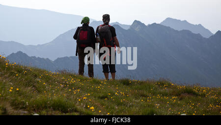 Couple of hikers admiring view and taking photographs of high mountains Stock Photo