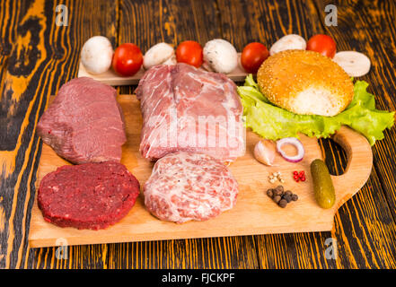 Raw red meat, peppers, garlic, tomato, bun and other ingredients for sandwich making laid out on cutting board Stock Photo