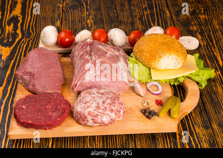 Wooden cutting board with various meat types for cheese and lettuce sandwich with tomato, mushroom, pepper and onion Stock Photo