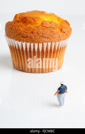 Overweight man looking up at an enormously large muffin a portion size or obesity concept Stock Photo