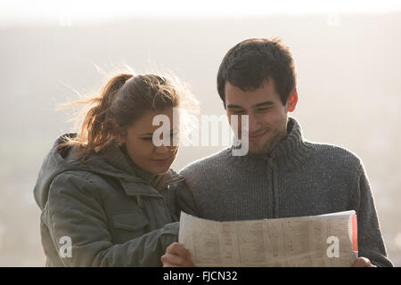 young couple, man and woman using map, standing in backlight Stock Photo