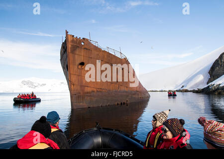 Antarctica tourism with cruise ship passengers in zodiac boat viewing old and historic whaling ship. Stock Photo